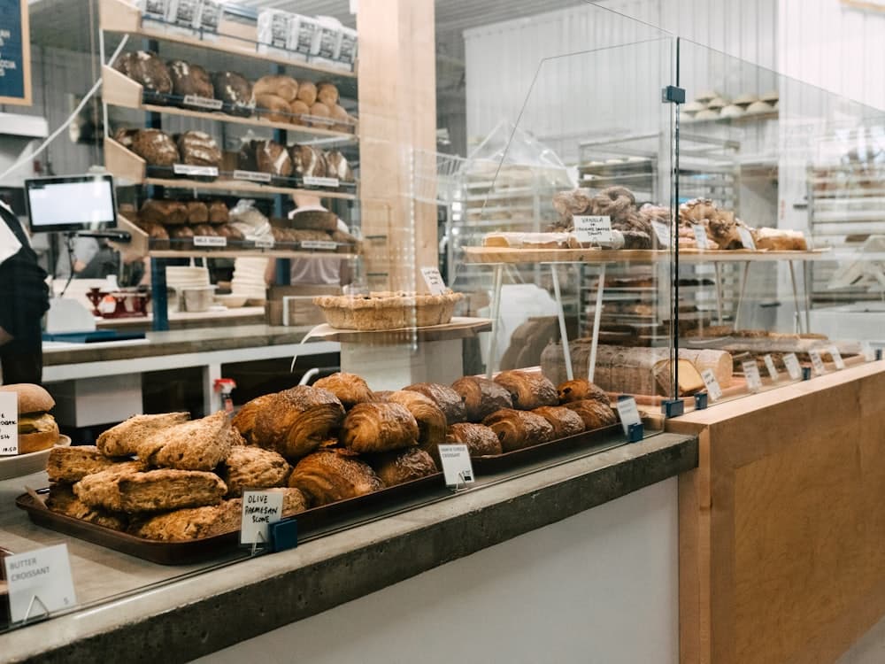 A bakery counter stacked with pastries, with shelves of bread loaves behind it.