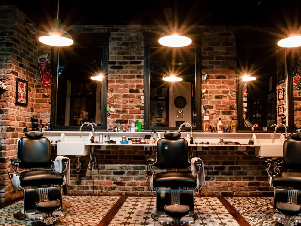 The interior of a barbershop, with leather chairs facing mirrors under warm pendant lights.