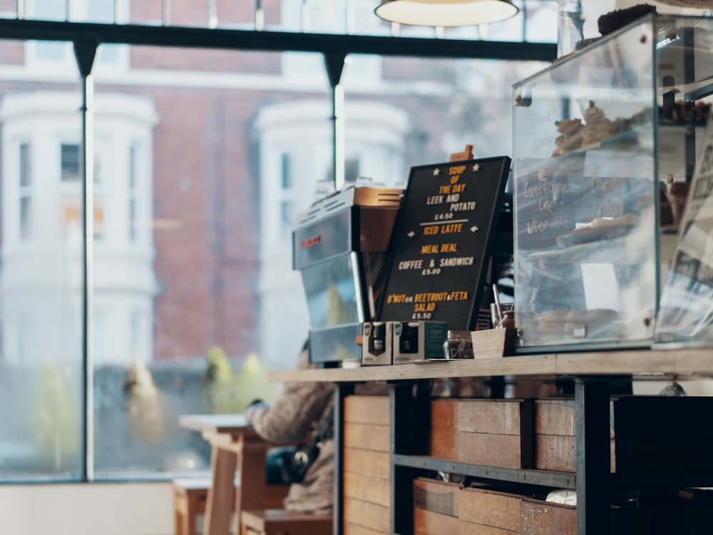 A café counter with an espresso machine and a chalkboard menu, looking out on to a street.
